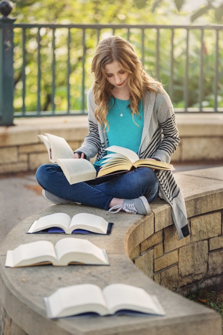 Senior girl reading multiple books at once outside in a park.