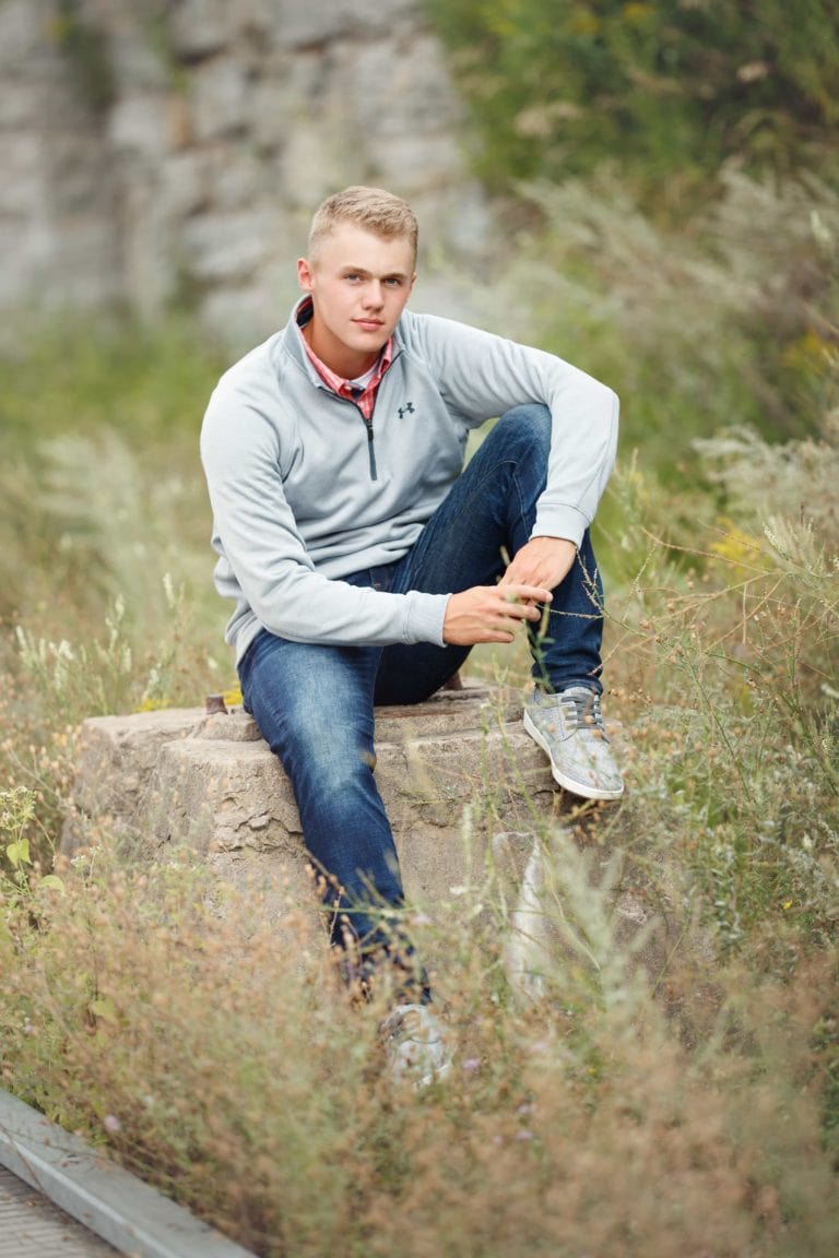 Senior guy poses on an old cement block in a field