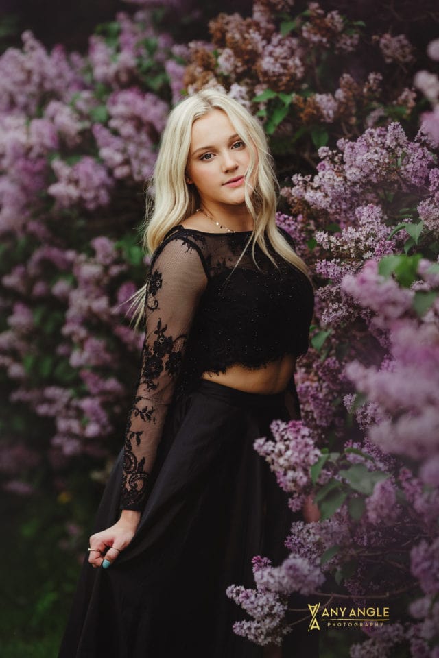 spring high school blonde senior in black dress standing in lilac bushes Any Angle Photography