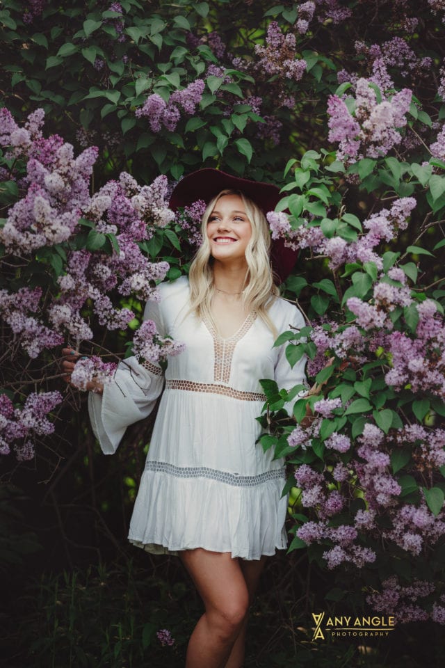 spring high school blonde senior in white dress standing in lilac bushes Any Angle Photography