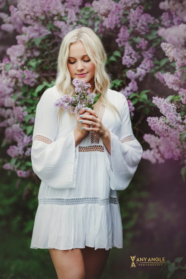 spring high school blonde senior in white dress standing in lilac bushes Any Angle Photography
