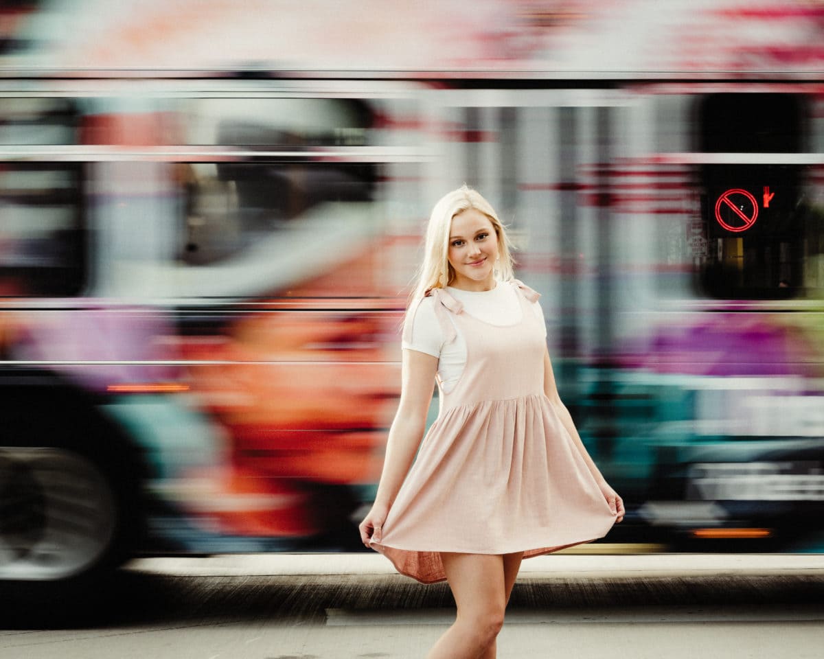 Urban senior pictures of girl standing in front of bus moving behind her.