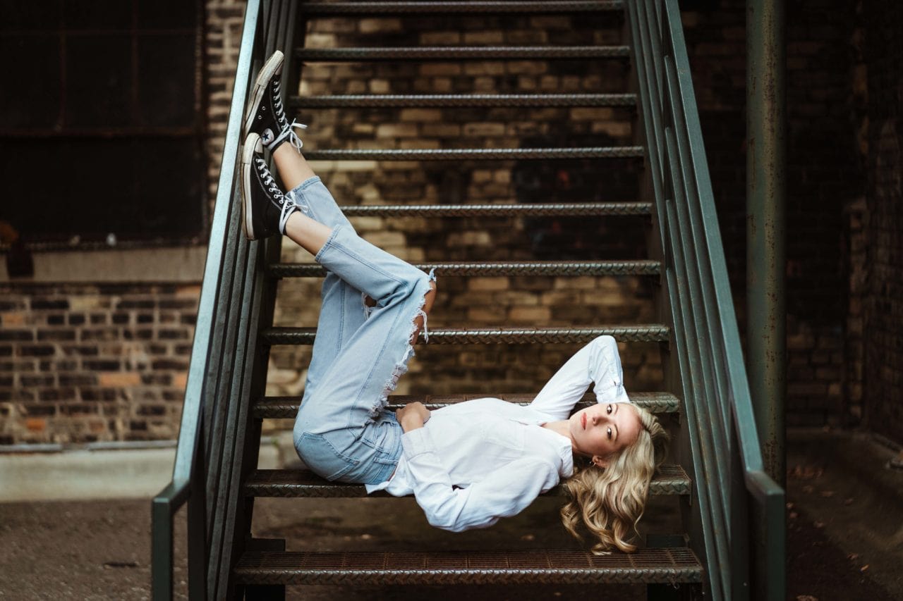 Senior girl lying down on an old staircase downtown.