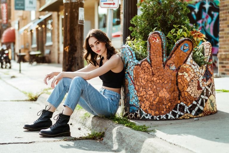senior girl sitting on city street curb leaning against a mosaic planter