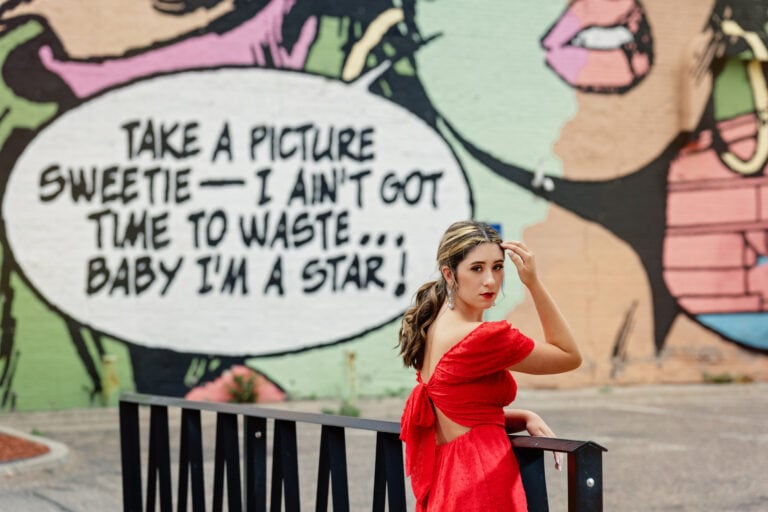 Urban Senior pictures with girl in red dress standing in front of a large mural in downtown Minneapolis. Captured by Minnesota senior photographer Any Angle Photography.