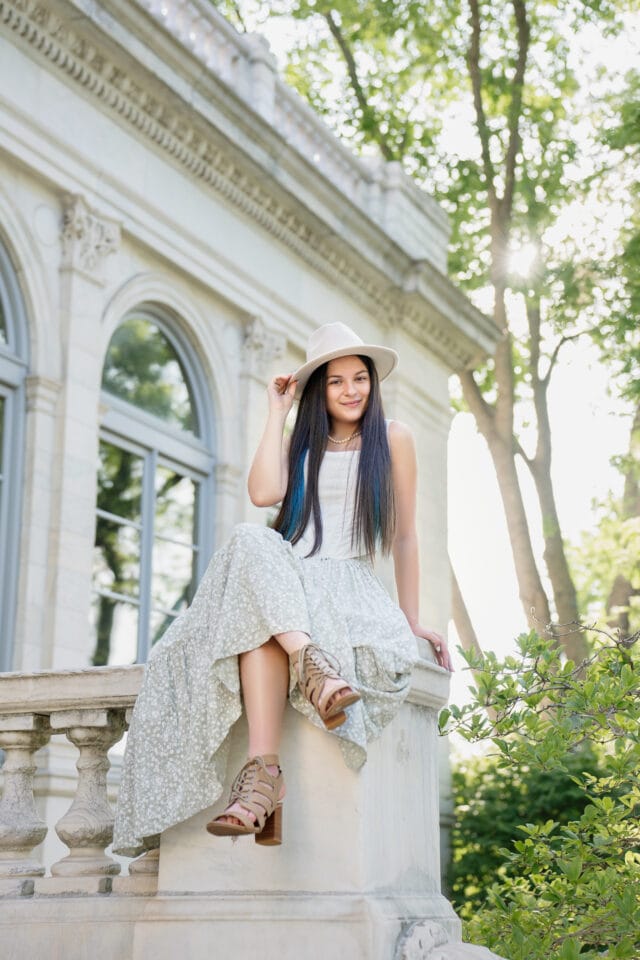 Senior pictures with girl sitting in front of urban white building by St Anthony Main. Captured by Any Angle Photography.