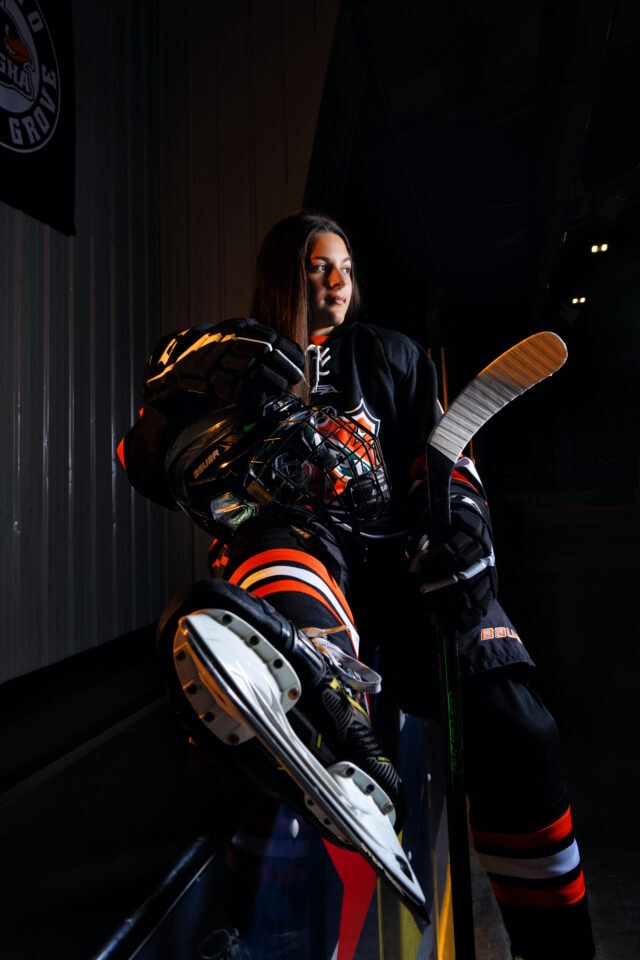 Senior pictures with hockey player sitting on railing at Osseo High School in Minneapolis. Captured by Any Angle Photography.