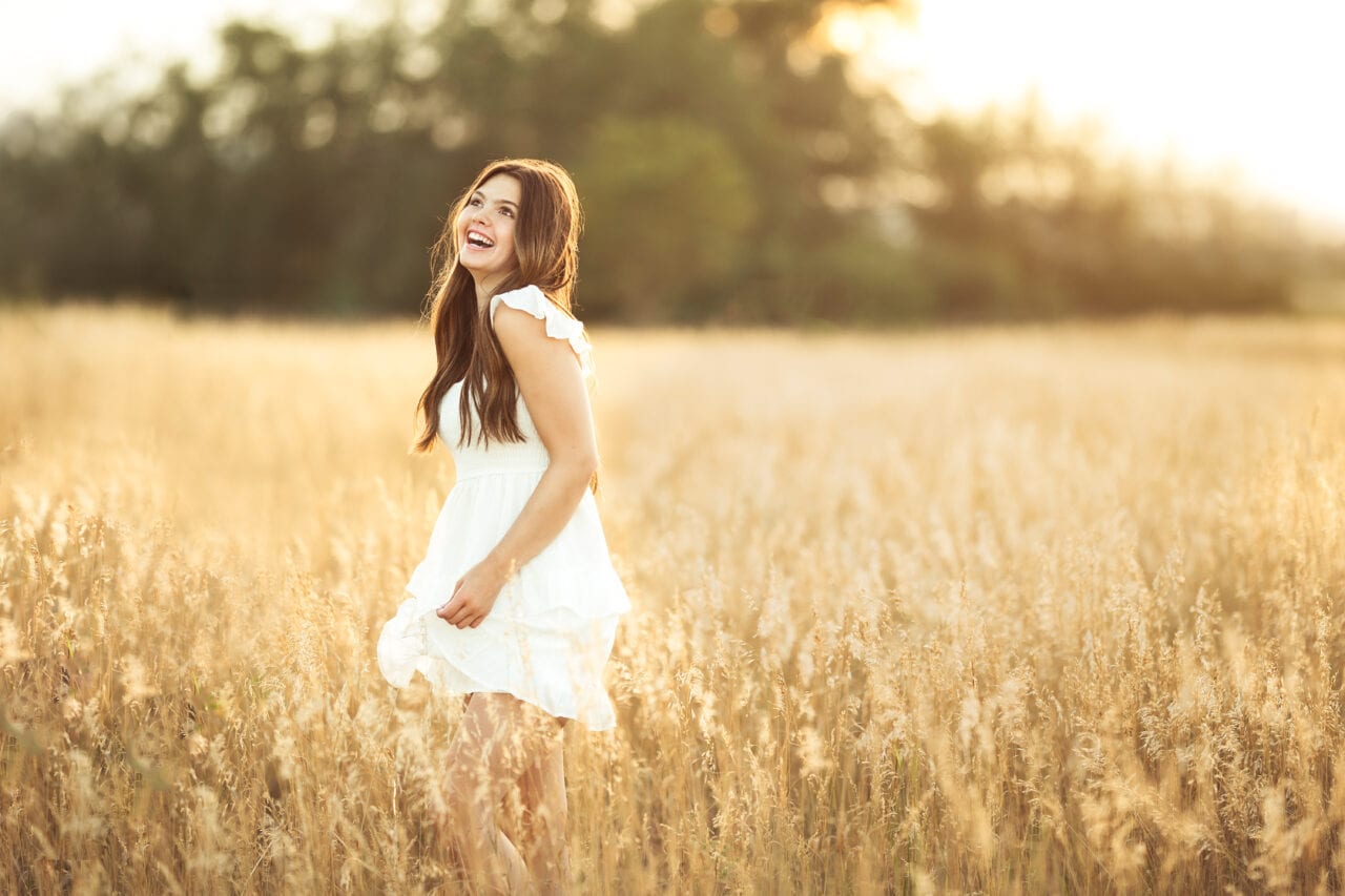 Nature senior pictures with girl in white dress standing in wheat field laughing. Captured by Minneapolis senior photographer Any Angle Photography.