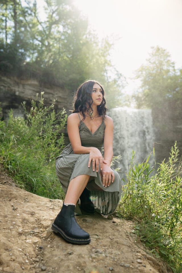 Nature senior pictures with girl in green dress squatting in front of Minnehaha Falls in Minnesota. Captured by Minneapolis senior photographer Any Angle Photography.