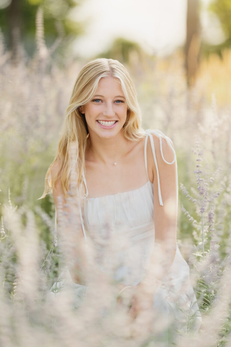Outdoor senior pictures with girl in white dress kneeling in flower field. Captured by Minneapolis senior photographer Any Angle Photography.